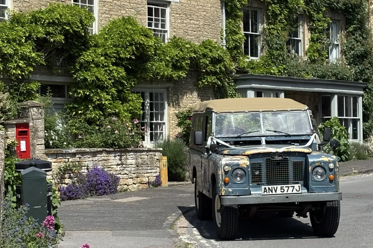 Our 1971 Land Rover Series 2a dressed with white wedding ribbons on a honey-stone village street
