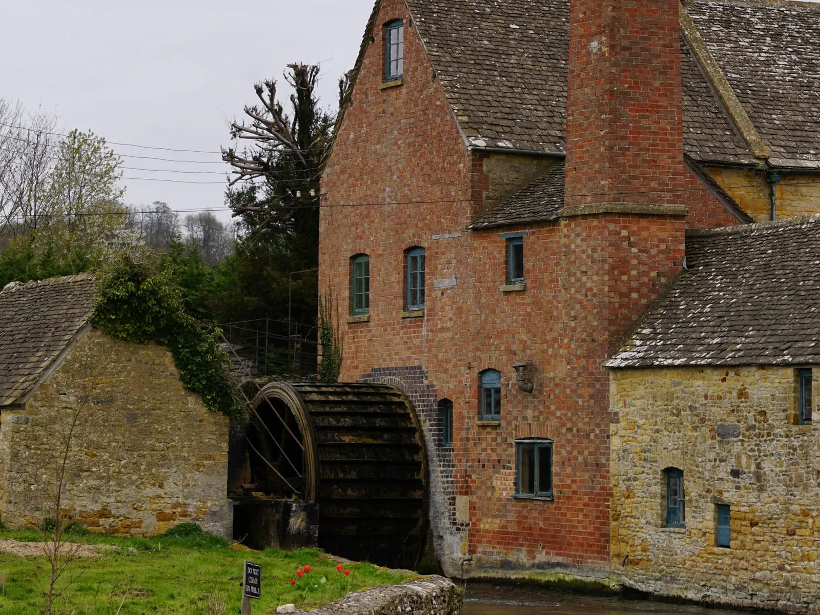 The red-brick Old Mill at Lower Slaughter with its waterwheel turning beside the River Eye